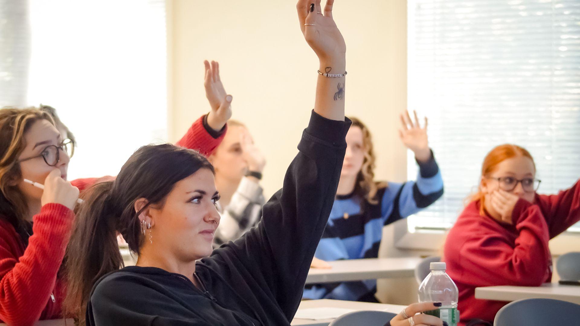 Student in front of room raising hand to ask a question